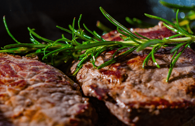 Two grilled steaks with a sprig of resemary on top